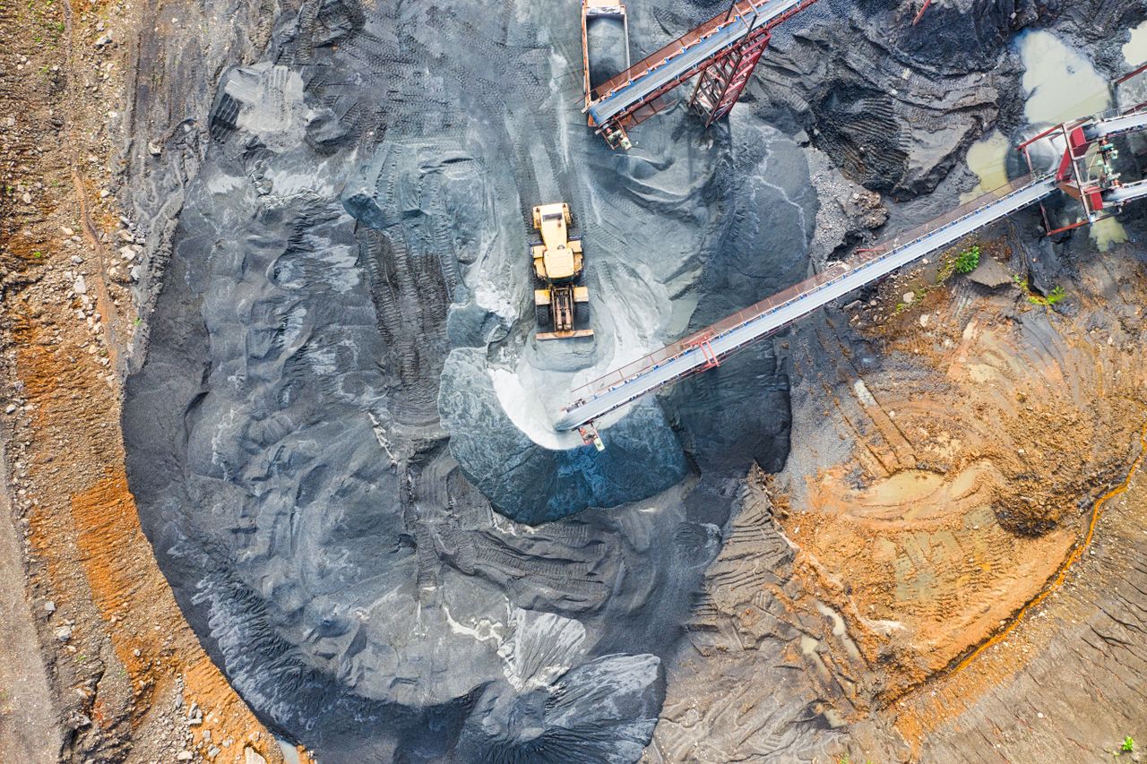 An aerial shot of an open-pit mine with machinery and pathways visible, surrounded by landscape.