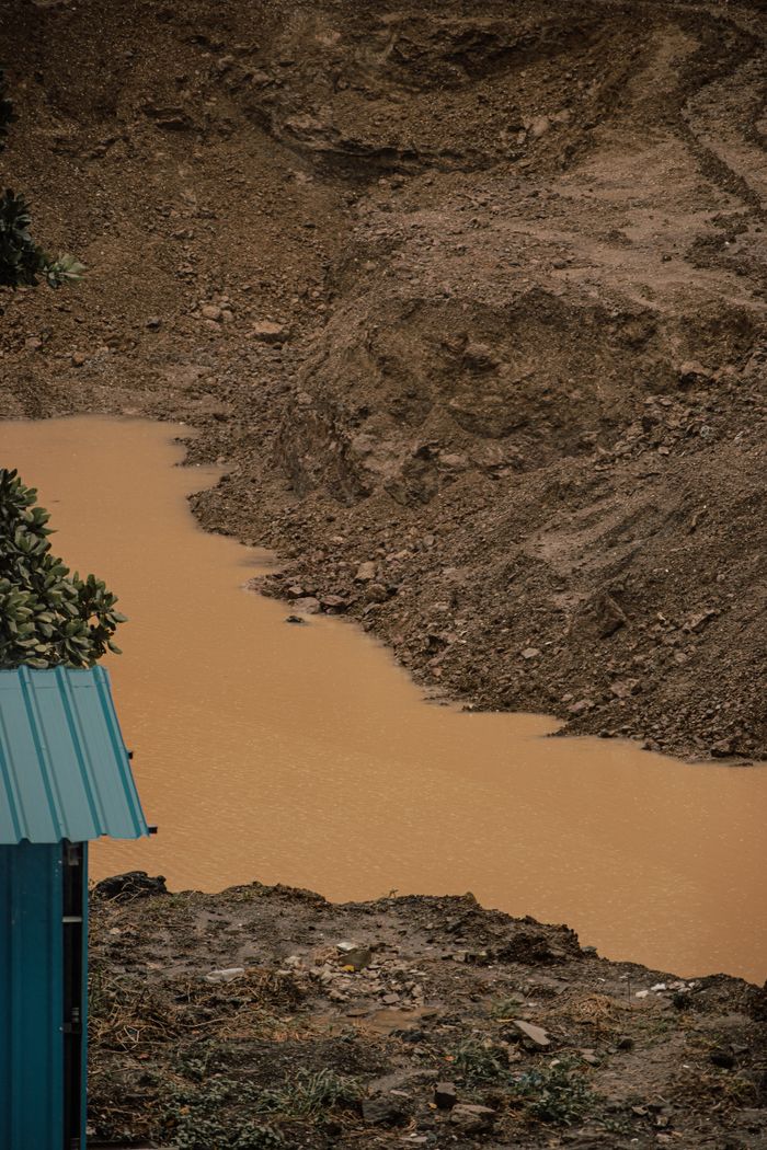 A rugged landscape with muddy water, blue metal roof, and sparse vegetation.